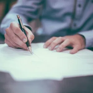 A person in a light blue shirt signing a document with a pen